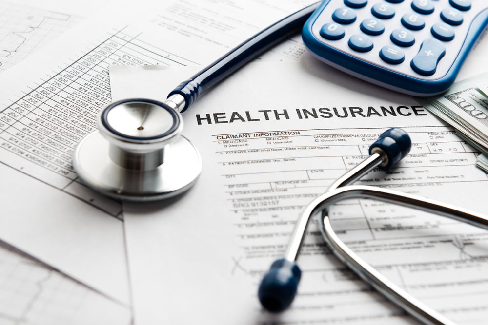 Stethoscope, calculator, and money lying on top of health insurance paperwork